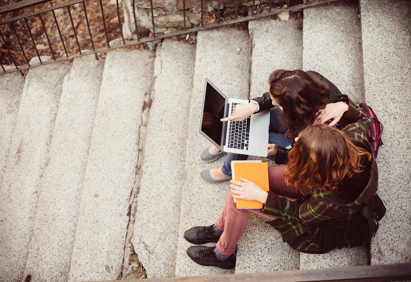 Two students writing and collaborating on a laptop